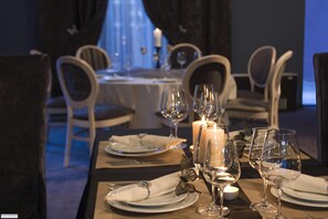 Mesa de jantar posta para uma refeição, com velas, copos de vinho e pratos.