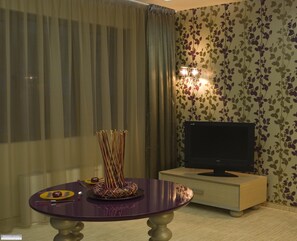 A room with a television on a stand, a table with a decorative centerpiece, and a wall with floral wallpaper. - Ores Boutique Hotel (Bansko)