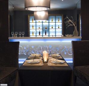 A dining area with a table set for four, a candle centerpiece, and a shelf with bottles and glasses behind the table. - Ores Boutique Hotel (Bansko)