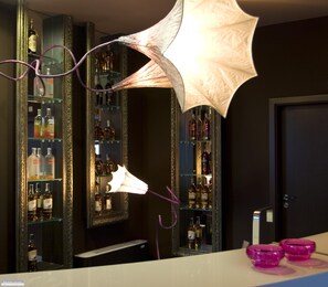 Un coin bar avec des étagères remplies de bouteilles d’alcool, un parapluie décoratif et des verres roses posés sur le comptoir.