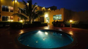 A pool surrounded by a building with multiple windows and a palm tree. - Ramee Dream Resort Seeb (Seeb)