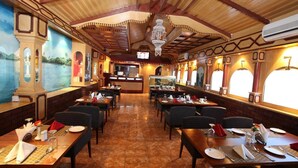 A restaurant with a high ceiling, wooden beams, and a mural on the wall. Tables are set with plates, glasses, and cutlery. - Ramee Dream Resort Seeb (Seeb)