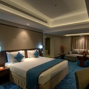 A hotel room with a large bed, a sofa, a small table with a vase, and a bathroom visible through an open door. - Ramee Dream Resort Seeb (Seeb)