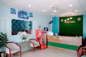 A reception desk with a green backdrop, a refrigerator, and a window with a metal grid. - D View Hotel (Mersing)