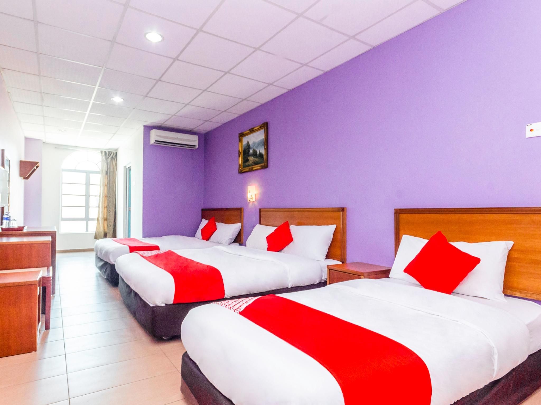 A hotel room with three beds, each with white and red bedding, a wooden headboard, and a nightstand.