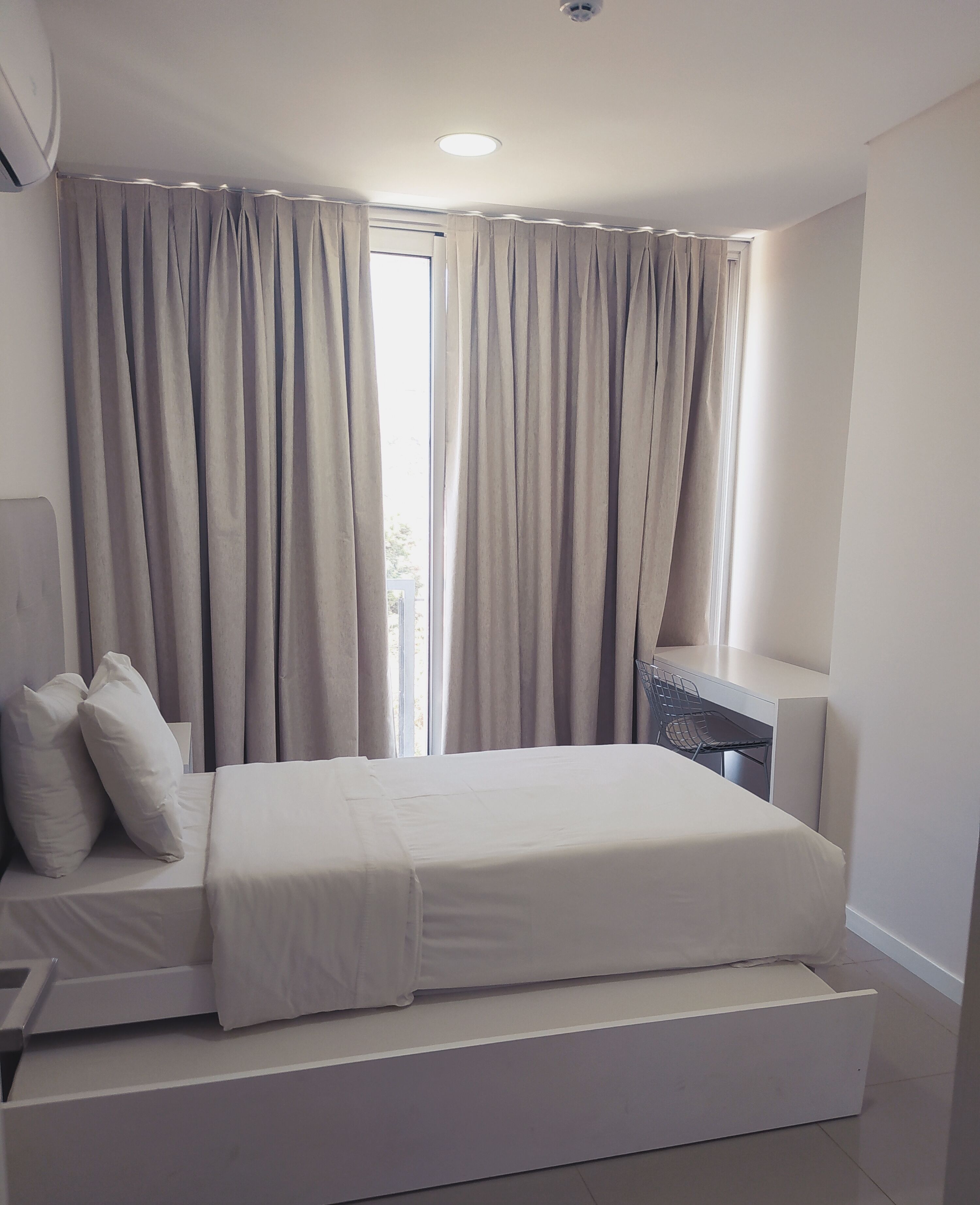 Une chambre à coucher moderne avec un lit, des rideaux, un bureau et une chaise.