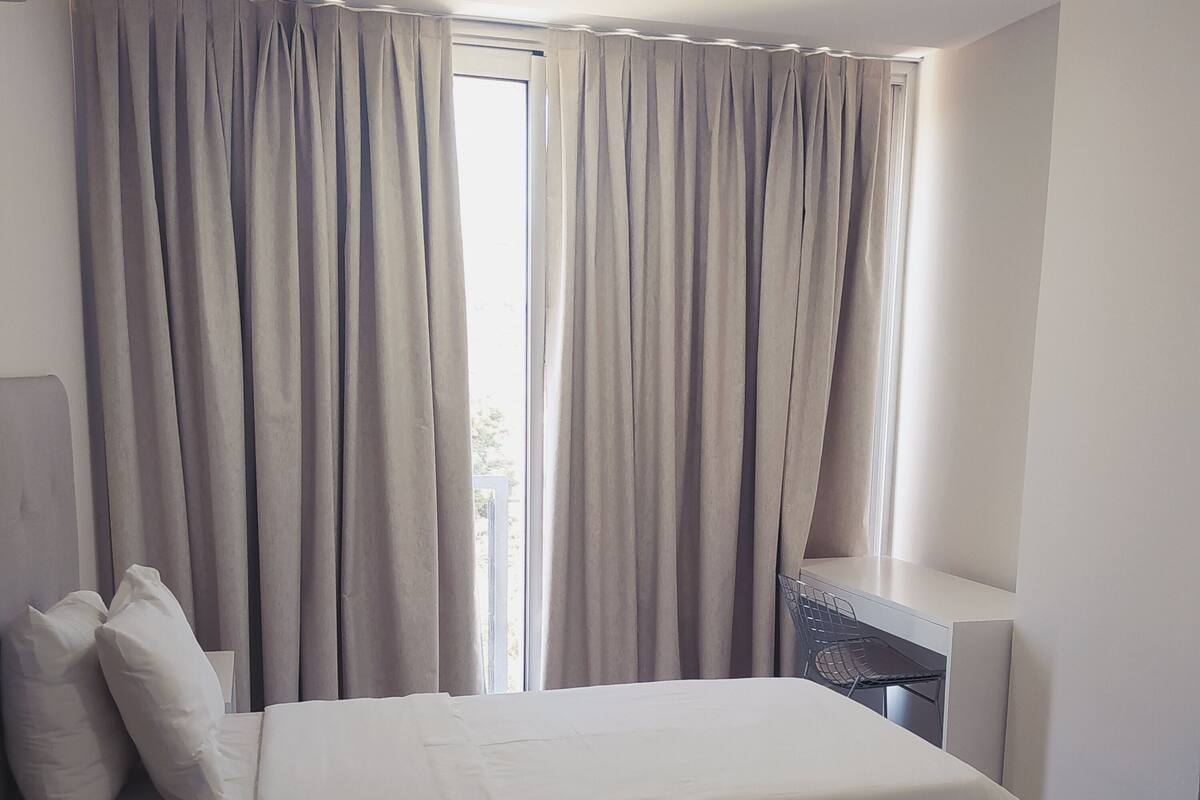 A modern bedroom with a bed, curtains, a desk, and a chair.