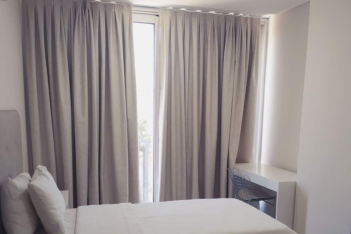 A modern bedroom with a bed, curtains, a desk, and a chair.