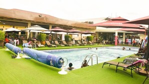 Un área de piscina con sillones de descanso y sombrillas, rodeada por un edificio con techo rojo.