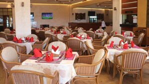 Un comedor con sillas y mesas de mimbre, cada juego con servilletas y cubiertos rojos.