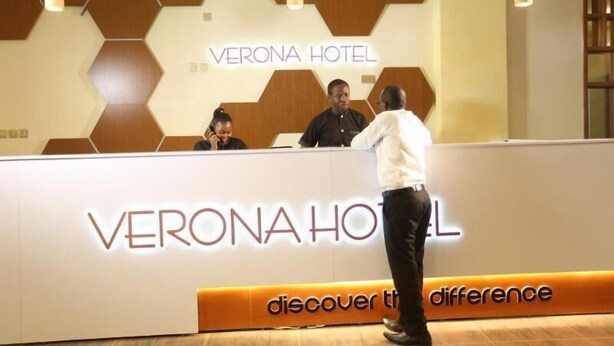 Mostrador de recepción en el Hotel Verona con un diseño moderno, que presenta patrones geométricos en la pared y el nombre del hotel bien visible.
