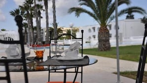 A table set outdoors with a chair, palm trees, and a building in the background.