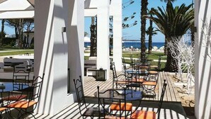 An outdoor patio area with tables and chairs, overlooking a beach and palm trees.