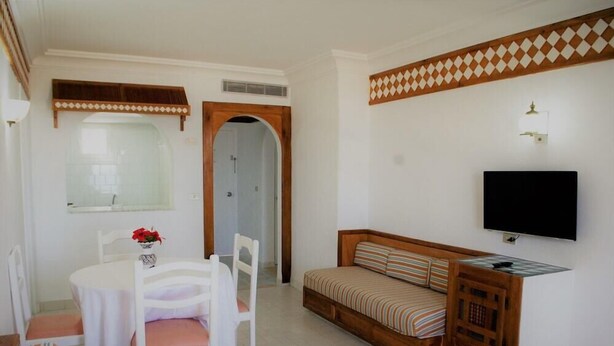 A compact living space with a dining table, chairs, a sofa, a TV, and a decorative wall panel.