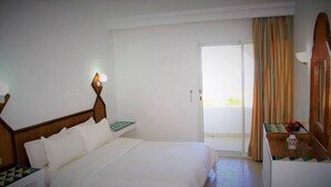 A hotel room with a bed, a nightstand, a lamp, a window with curtains, and a view of the outside.