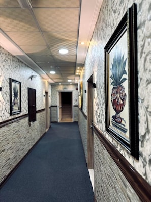 Um corredor com paredes estampadas, obras de arte emolduradas e piso coberto por carpete.
