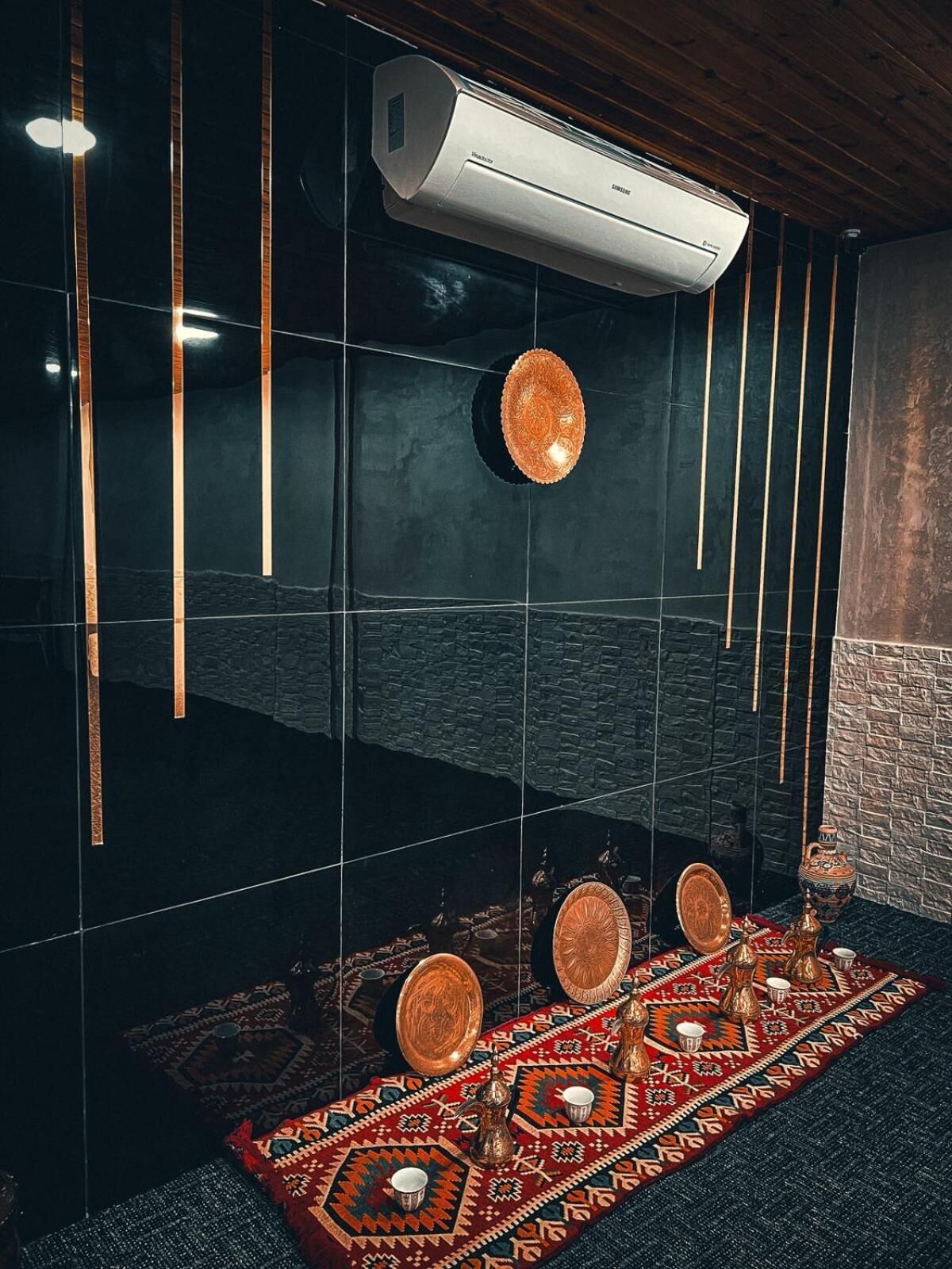 A modern room with a black tiled wall, a patterned rug, a traditional tea set, and an air conditioning unit.