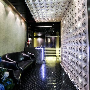 A hotel lobby with a reception desk, a seating area with chairs, and a textured wall. - Khuttar Furnished Apartments (Amman)