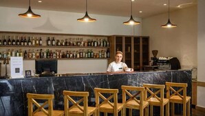 A bar area with a marble counter, wooden chairs, and a bartender. - Aurora Resort by One Hotels (Tsaghkadzor)