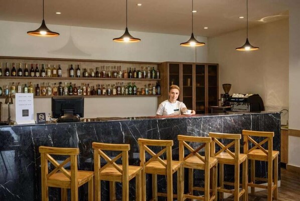 Zona de bar con mostrador de mármol, sillas de madera y un barman.