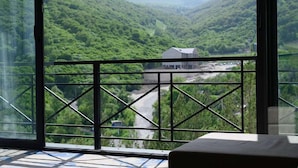 A room with a large window offering a view of a lush valley and a building in the distance. - Aurora Resort by One Hotels (Tsaghkadzor)