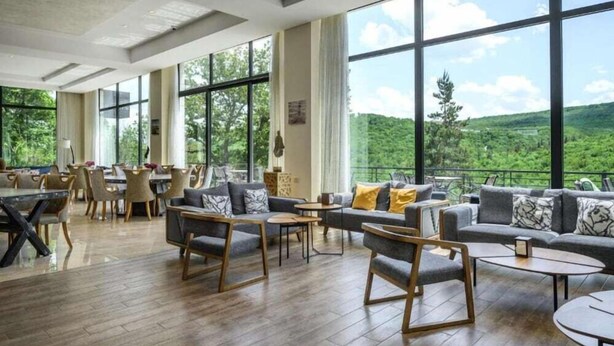 A spacious indoor area with large windows offering a view of a forested landscape. - Aurora Resort by One Hotels (Tsaghkadzor)