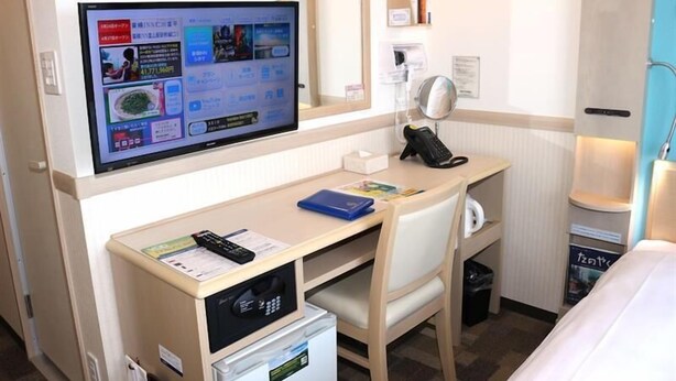 Een hotelkamer met een bureau, een televisie, een telefoon en een kleine koelkast.