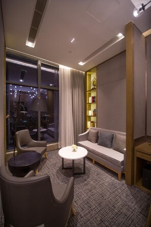 A modern hotel room with a sofa, two chairs, a small round table, a bookshelf, and a large window offering a city view. - Xiamen Zenith Hotel (Xiamen)