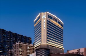 A modern high-rise building with a curved facade and illuminated signage. - Xiamen Zenith Hotel (Xiamen)