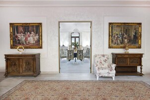 Una habitación con dos armarios de madera ornamentada, un sillón floral y dos cuadros clásicos en las paredes.