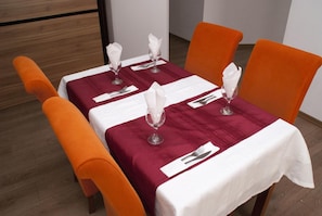 Una mesa de comedor con manteles blancos, sillas color naranja y cubertería y servilletas ordenadas.