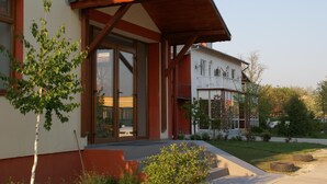 A modern house with a wooden porch, large sliding glass doors, and a small garden area with a tree and bushes. - Otopeni (Otopeni)