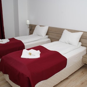 Dos camas individuales con ropa de cama blanca y mantas rojas, una mesita de noche con lámpara y un cabecero de madera.