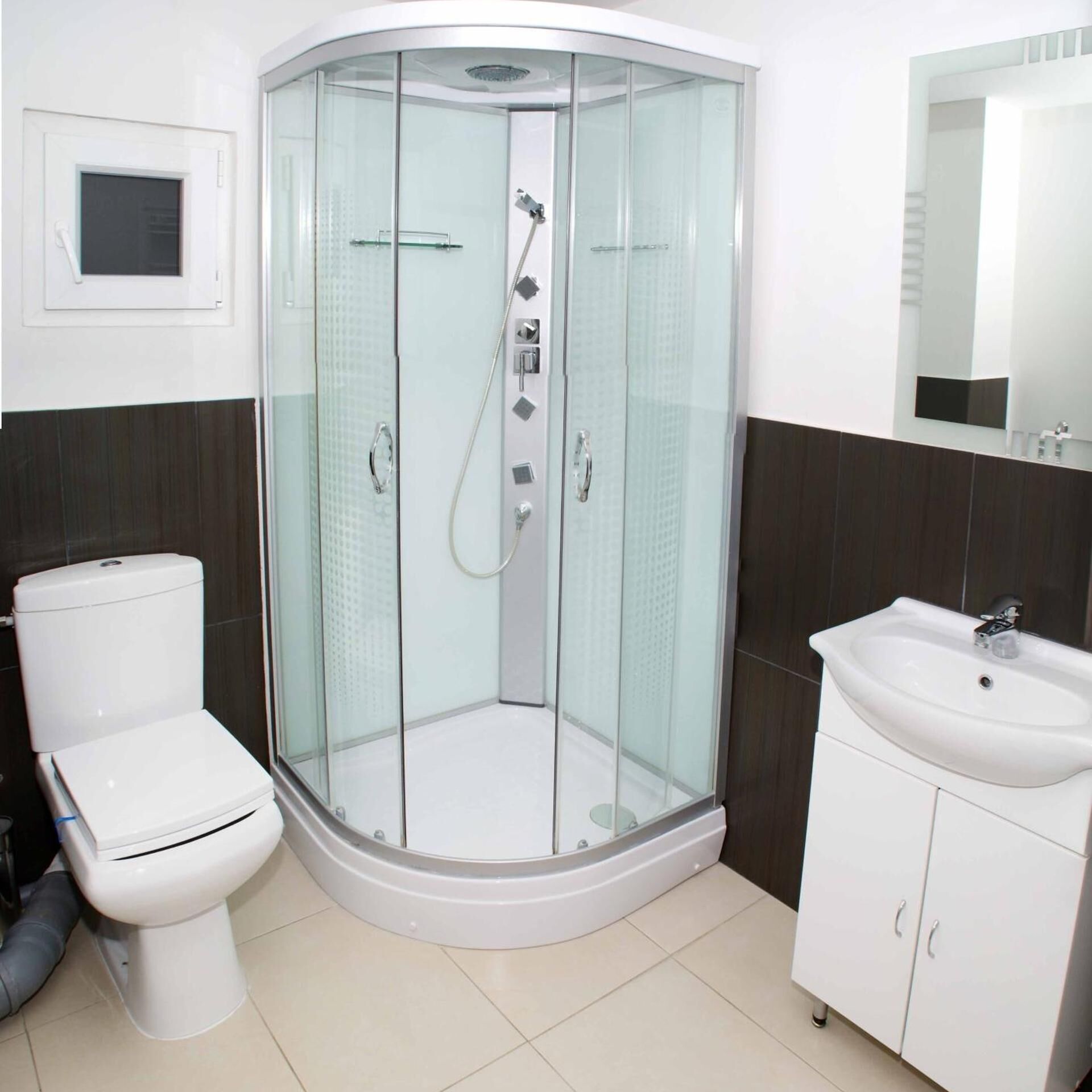 A corner bathroom with a glass-enclosed shower, a toilet, and a sink with cabinets.