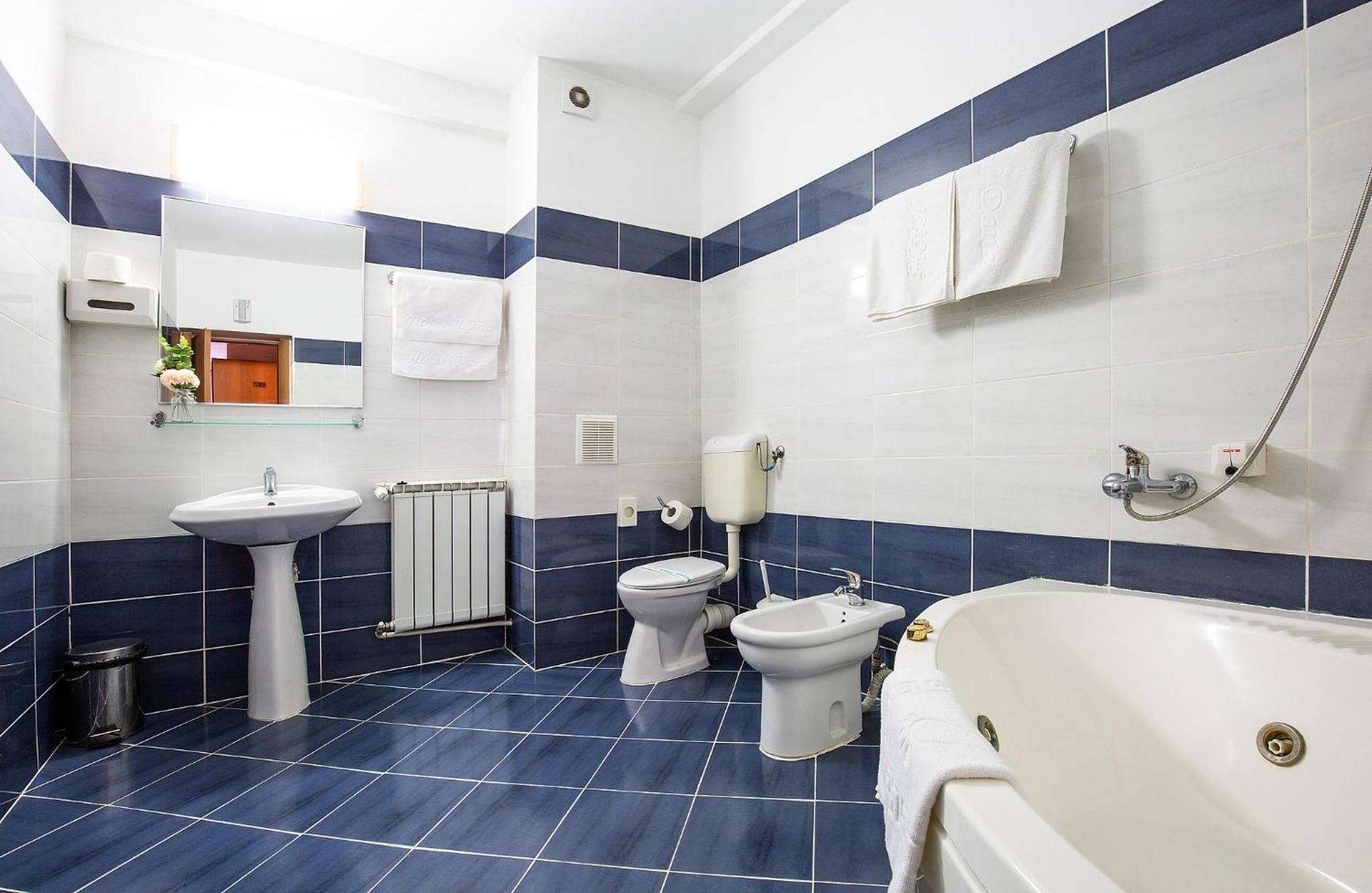 A modern bathroom with a white sink, toilet, and bathtub, blue-tiled walls, and a mirror above the sink.