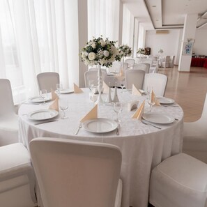 A formal dining room with round tables, white chairs, and a floral centerpiece. - Dana (Satu Mare)