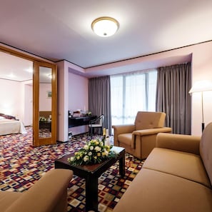 A hotel room with a bed, a desk, two armchairs, a coffee table with flowers, and a large window with curtains. - Hotel Mara (Sinaia)