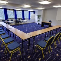 Un salón de conferencias con una larga mesa, sillas, una pizarra blanca y una planta.