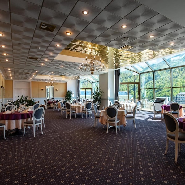 A spacious dining area with tables and chairs, large windows, and a chandelier. - Hotel Mara (Sinaia)