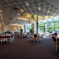Un comedor amplio con mesas y sillas, ventanas grandes y un candelabro.