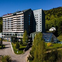 Un hotel de varios pisos con un diseño moderno, un área de estacionamiento y un paisaje verde con árboles.