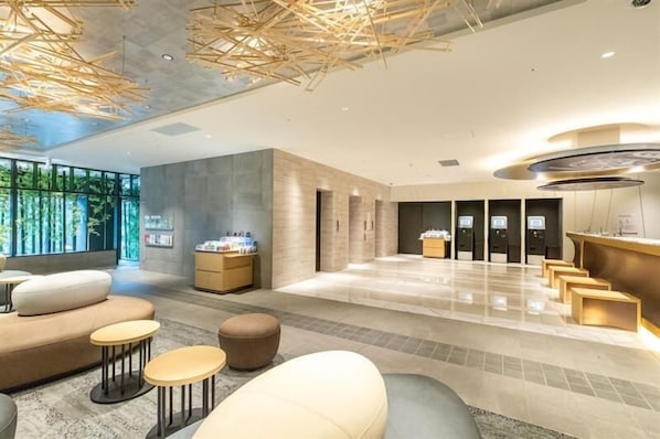 A modern lobby with seating areas, a reception desk, and a large window with a view of greenery.