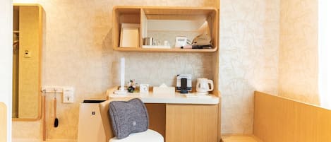 Habitación compacta y bien organizada, con un escritorio pequeño, una silla, una kitchenette integrada y un estante empotrado sobre el escritorio.