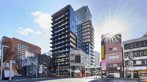A multi-story urban building with a modern architectural design, featuring a mix of glass and concrete facades, and a pedestrian-friendly street with shops and a crosswalk. - Daiwa Royal Hotel D City Nagoya Fushimi (Nagoya)