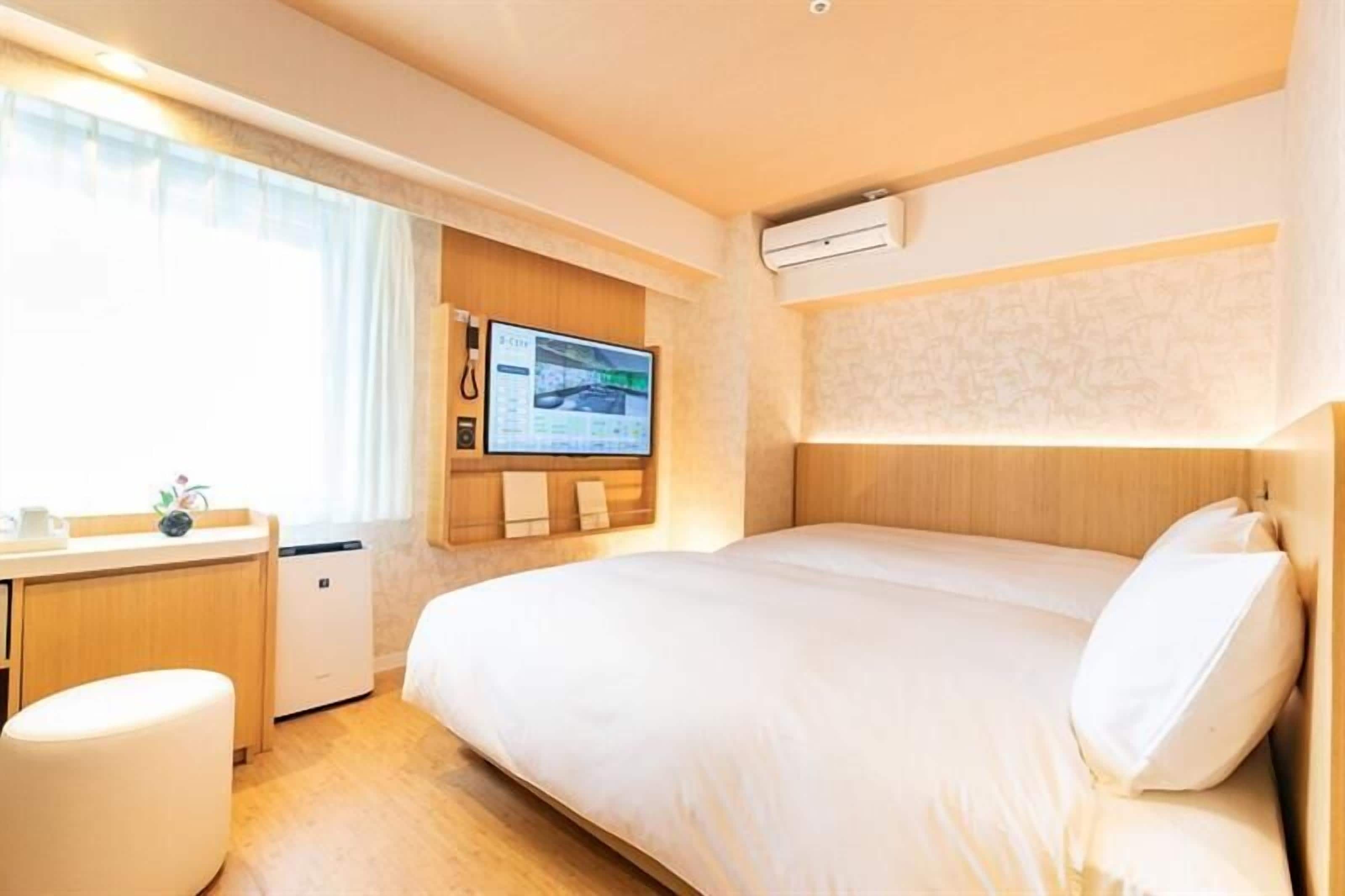 Habitación de hotel con cama, escritorio, kitchenette pequeña y televisor en la pared.