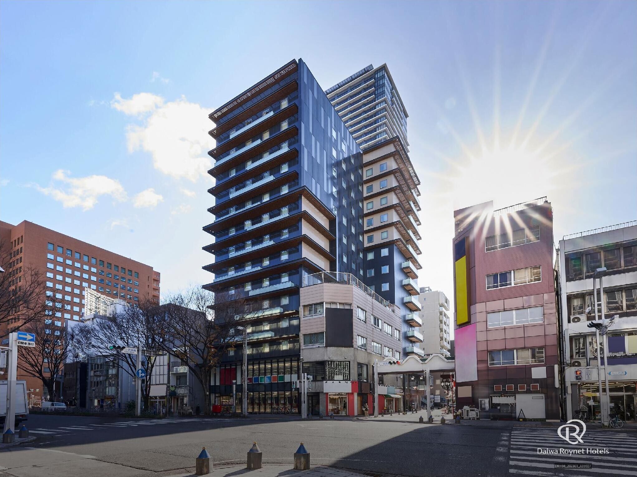 A modern hotel building with multiple floors, large windows, and a prominent entrance area with shops and outdoor seating.