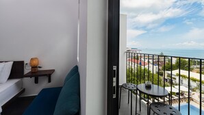 A balcony with a bed, a small table, and a view of the sea and buildings.