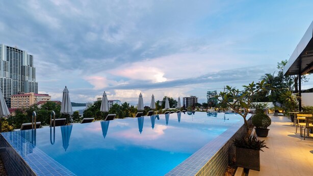 An infinity pool with a view of the city skyline, surrounded by umbrellas and potted plants.