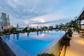 An infinity pool with a view of the city skyline, surrounded by umbrellas and potted plants. - Onederz Sihanoukville (Sihanoukville)