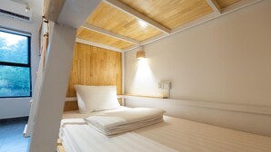 A modern hotel room with a wooden ceiling, a neatly made bed with white linens, a bedside table, and a window offering a view of the outdoors.